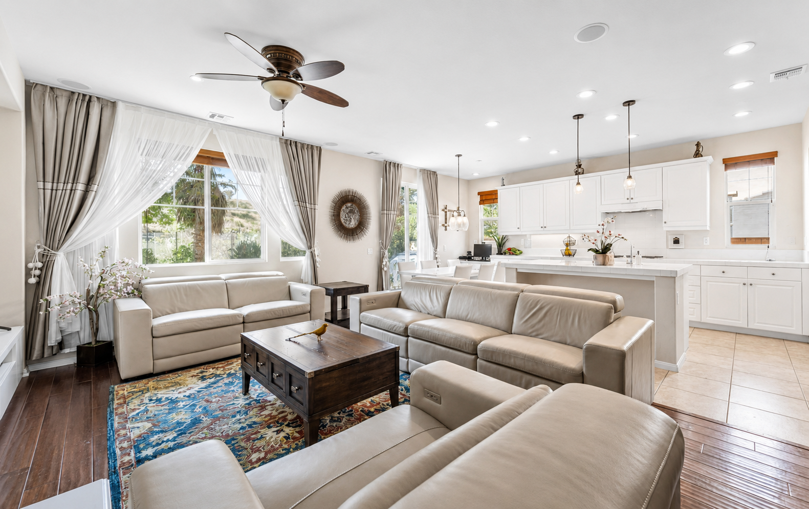 Bright living room with cozy seating, big windows, and an open kitchen nearby.