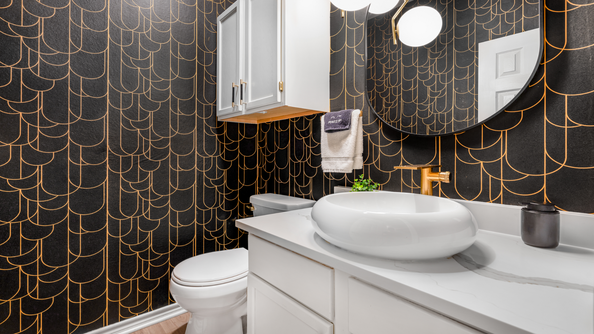 Step into this stylish powder room, where bold meets elegance. Black and gold wallpaper, a chic round mirror, and sleek fixtures create a luxe vibe—perfect for a quick refresh!