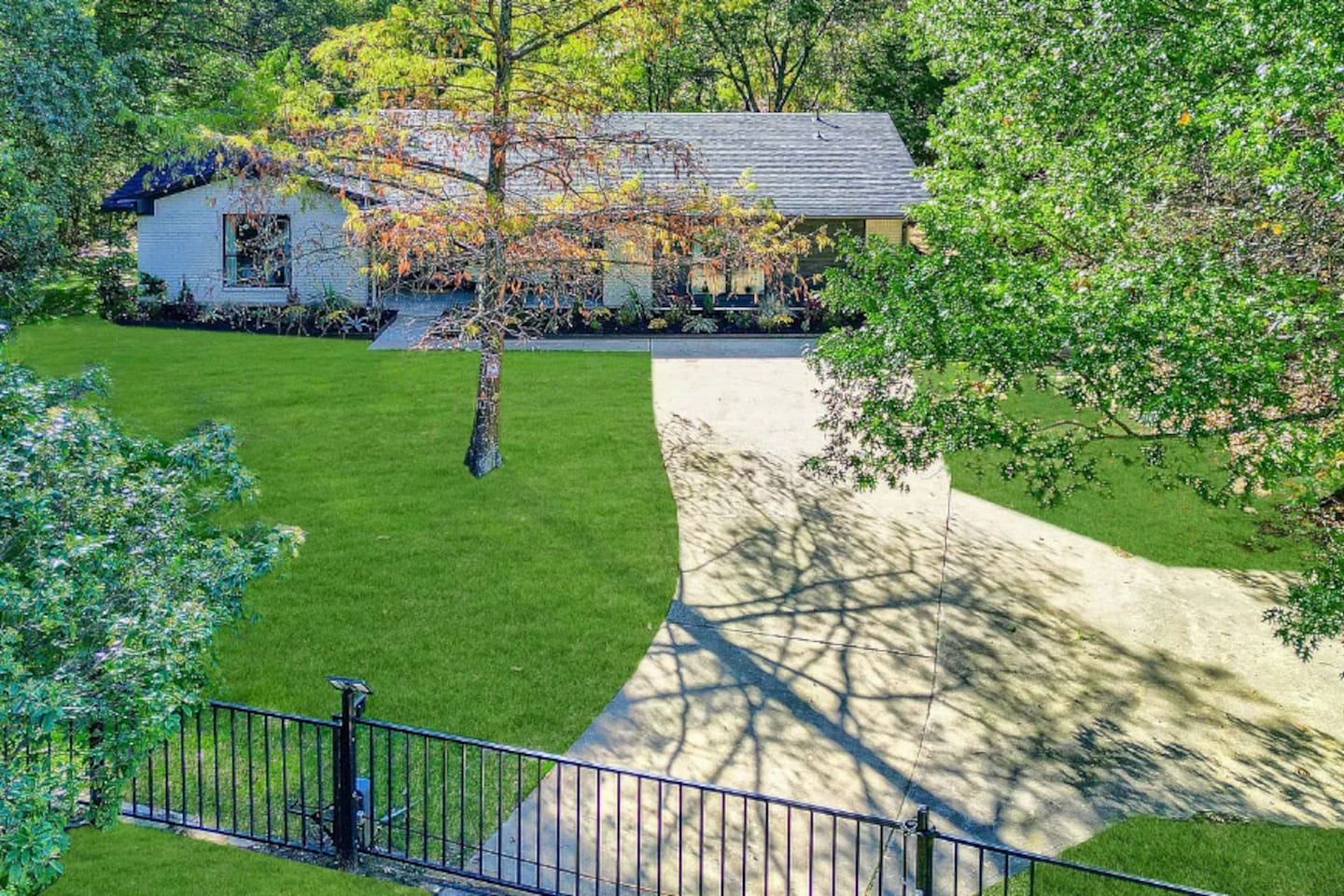 Elevated front approach showing the long driveway, manicured lawn, and secluded feel of the property.
