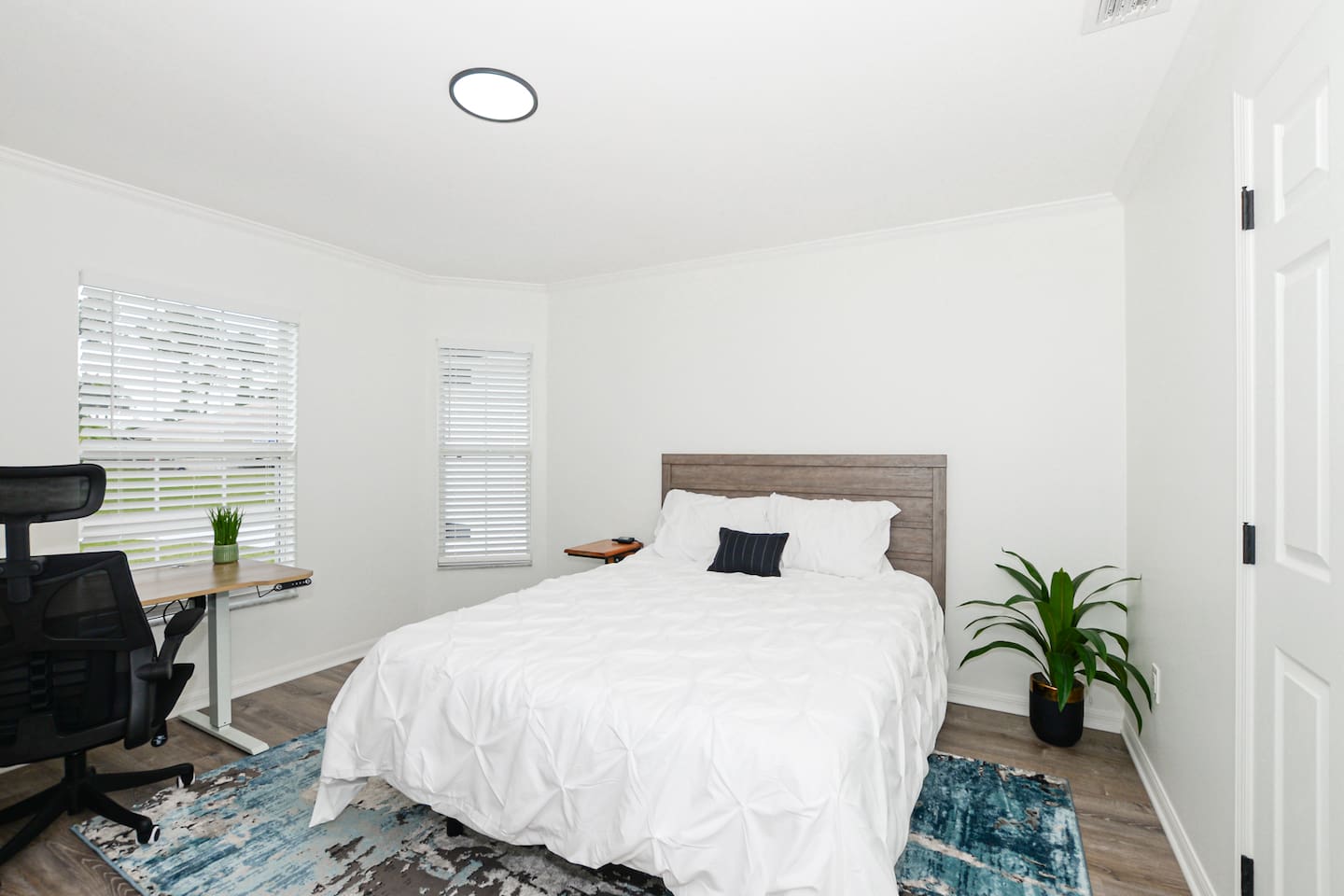 Spacious bed with a plant on the side and a dedicated workspace, offering both comfort and functionality.