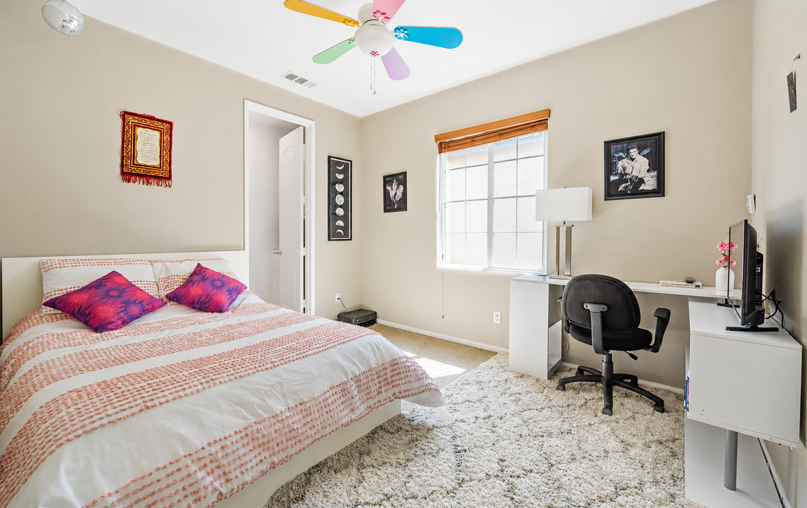 Bedroom with a comfortable bed, desk workspace, and a fun colorful ceiling fan.
