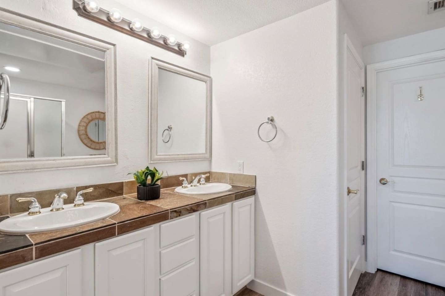 Bathroom vanity with double sinks, bright mirror lighting, cabinet storage, and easy access to the nearby shower.
