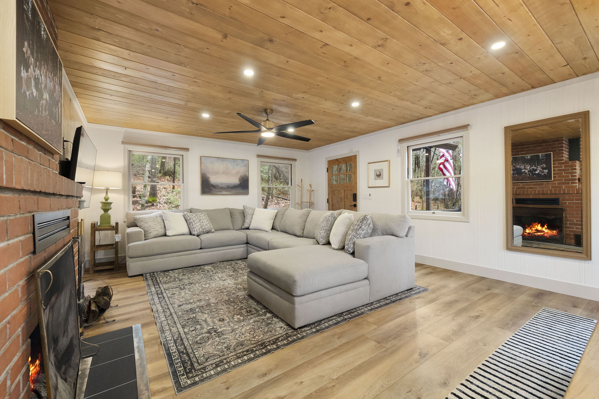 Spacious - yet cozy living room as you walk in. Showcasing a beautiful pine ceiling, lighting options, a large sofa, tv and wood burning fireplace.