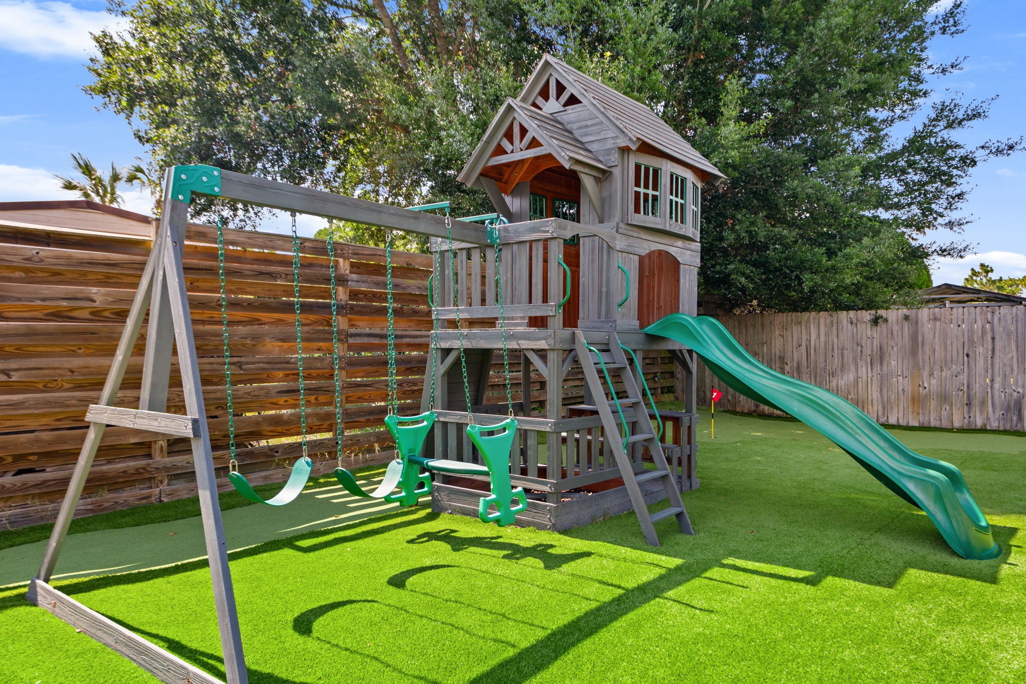 Let the kids run wild! Our private backyard features a premium wooden playset complete with a clubhouse fort, two belt swings, a double glider, and a wavy slide—all over clean, soft artificial turf for worry-free play.