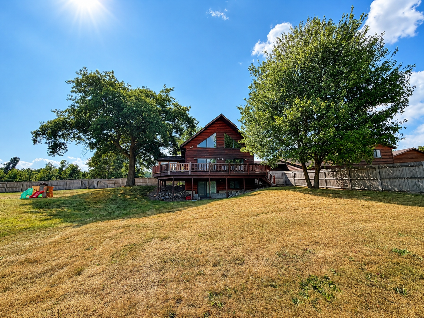 Wide exterior view shows the House surrounded by open lawn, mature trees and peaceful Wisconsin scenery.

