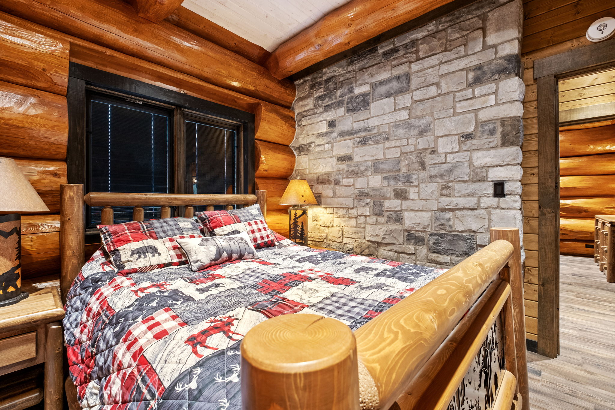 Cozy queen bedroom featuring a warm stone accent wall, handcrafted wooden furniture, and rustic lodge décor — perfect for a peaceful night’s rest.