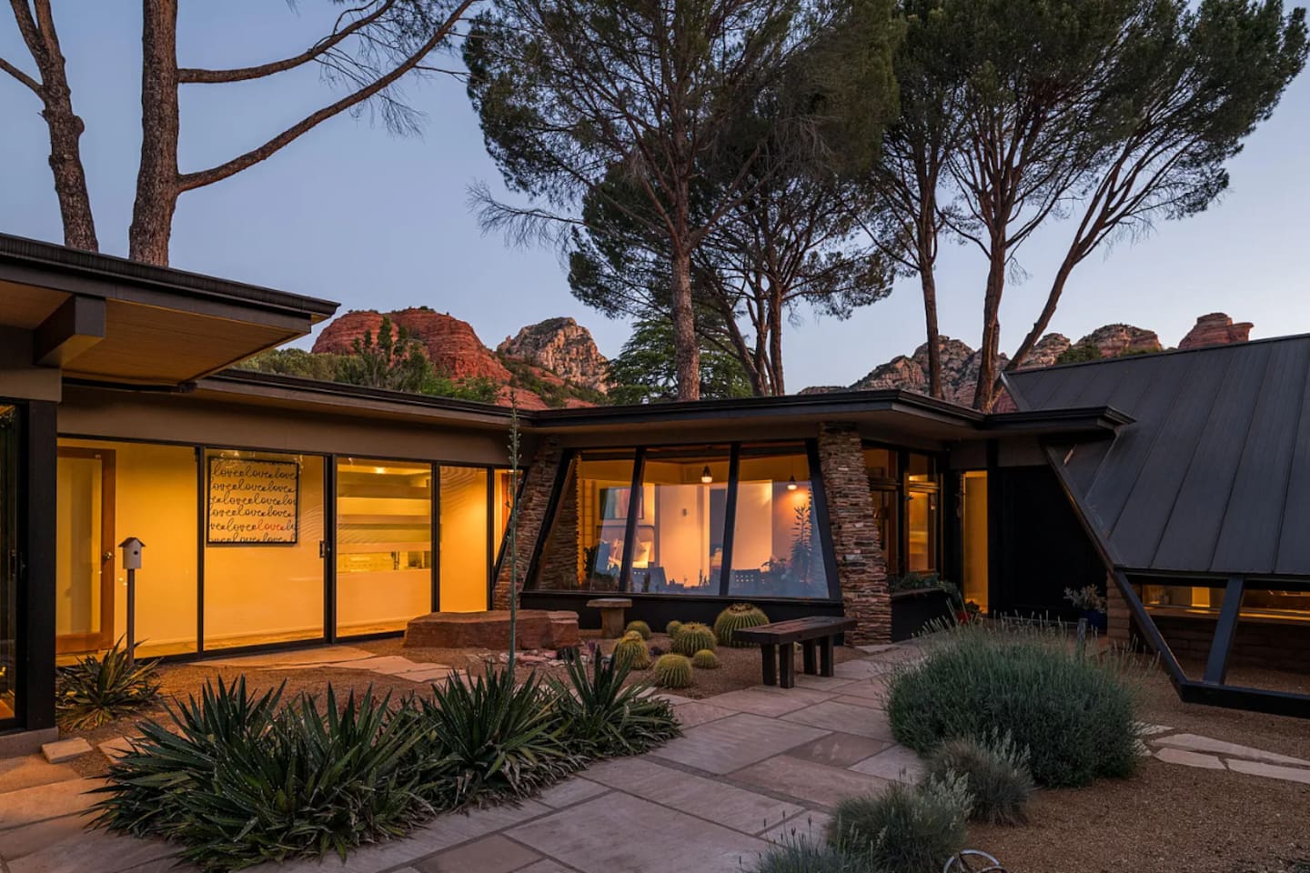 Mid-century elegance at dusk — warm interior glow, bold architectural lines, and Sedona’s red rocks rising just beyond.