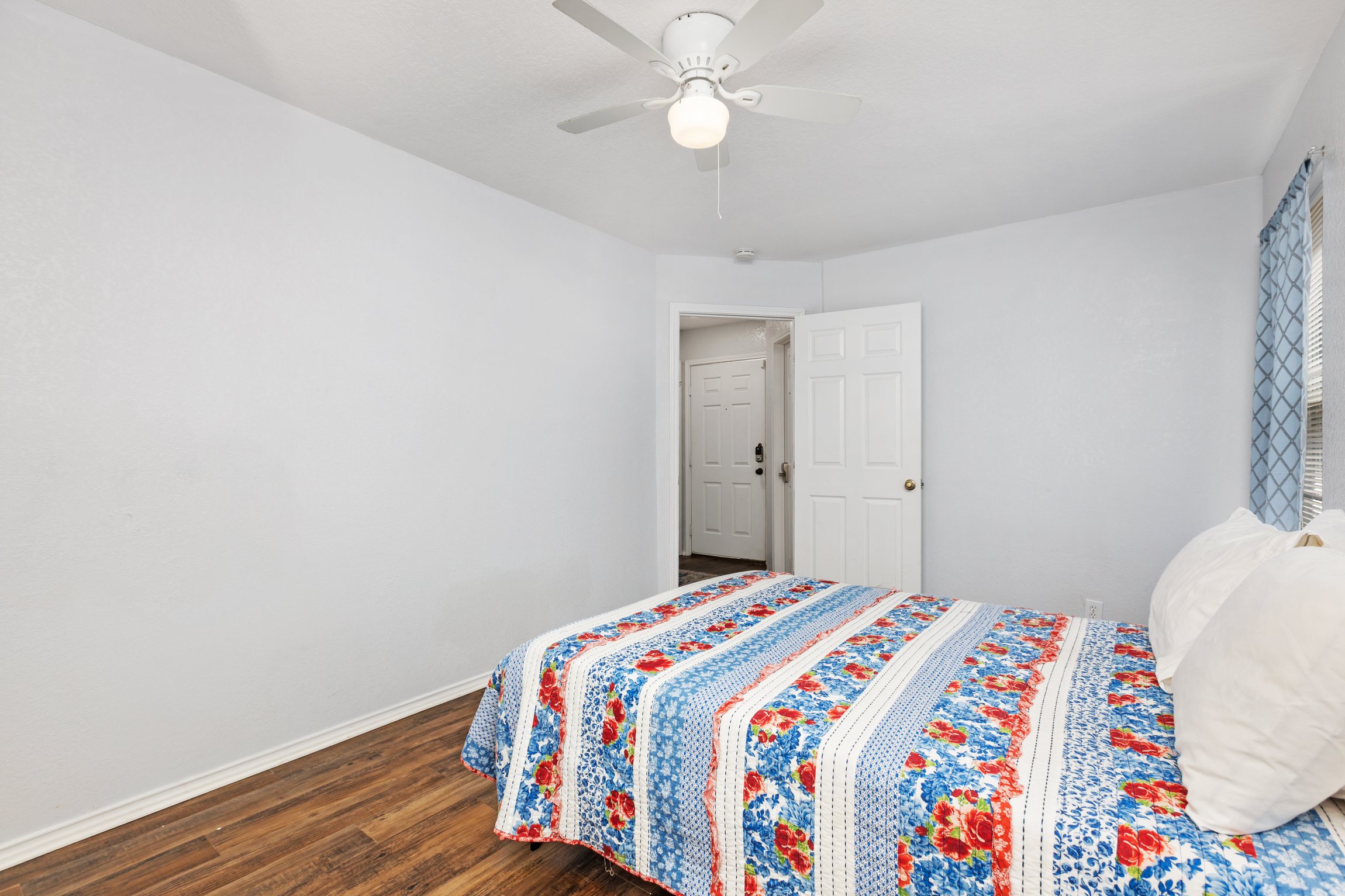 Spacious queen bedroom with colorful bedding, ceiling fan, closet storage, and hardwood floors. Hotel-quality cotton linens, extra pillows, and blankets provided. Current decorative blankets, bedding, and wall art are not shown in these photos.