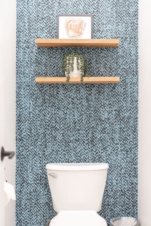 Stylish toilet nook with patterned accent wall and floating shelves.