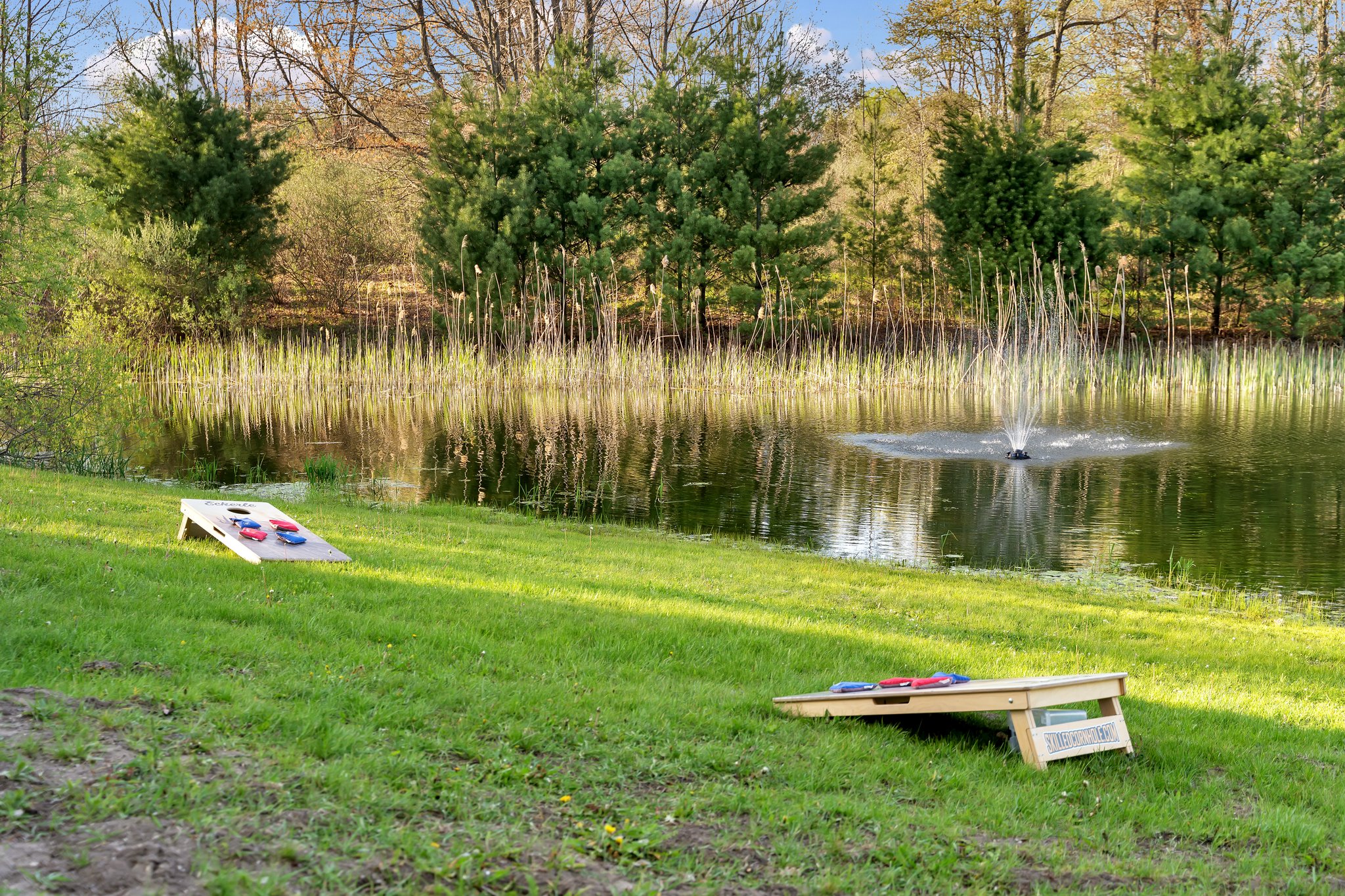 Pond water fountain with corn hole game on the shore.