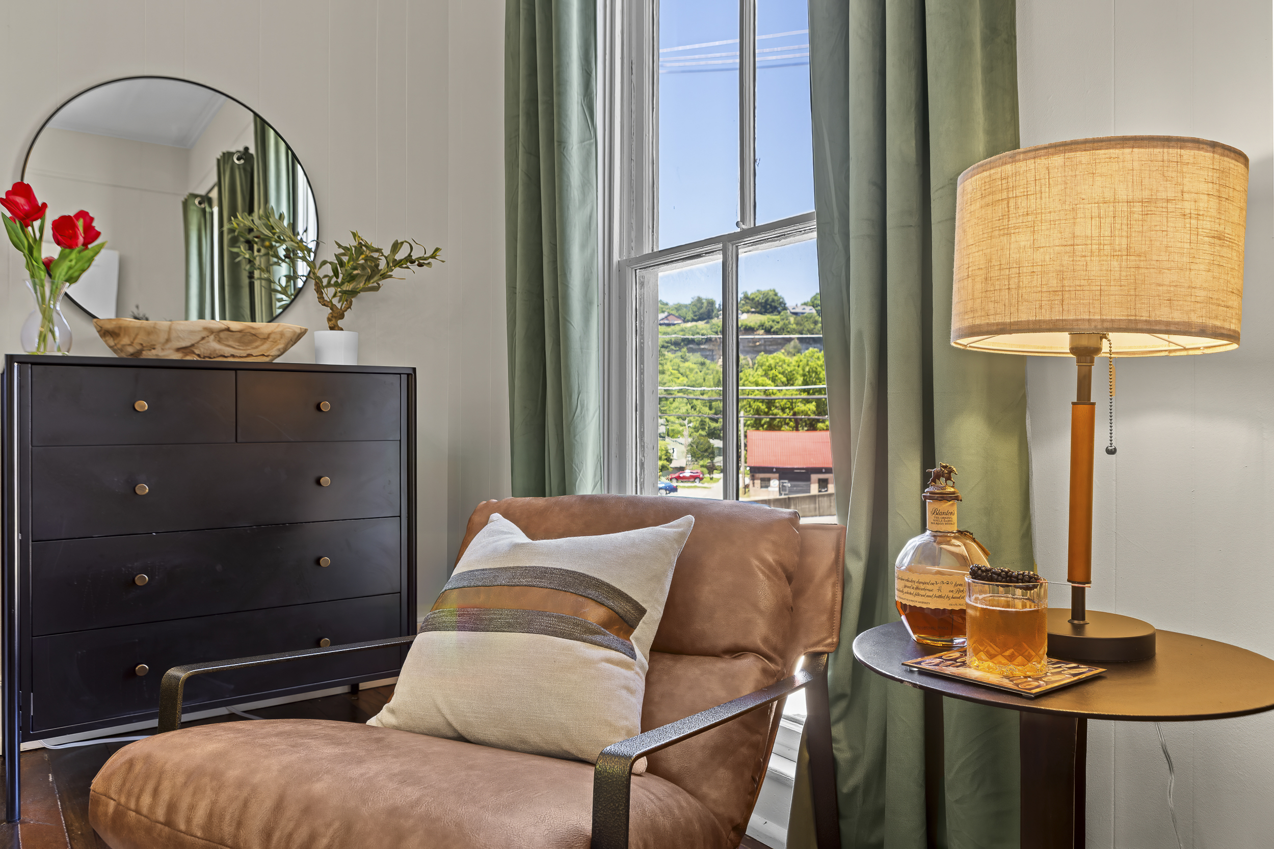 A private reading corner with a leather chair, morning light, and a view of green Frankfort hillsides.