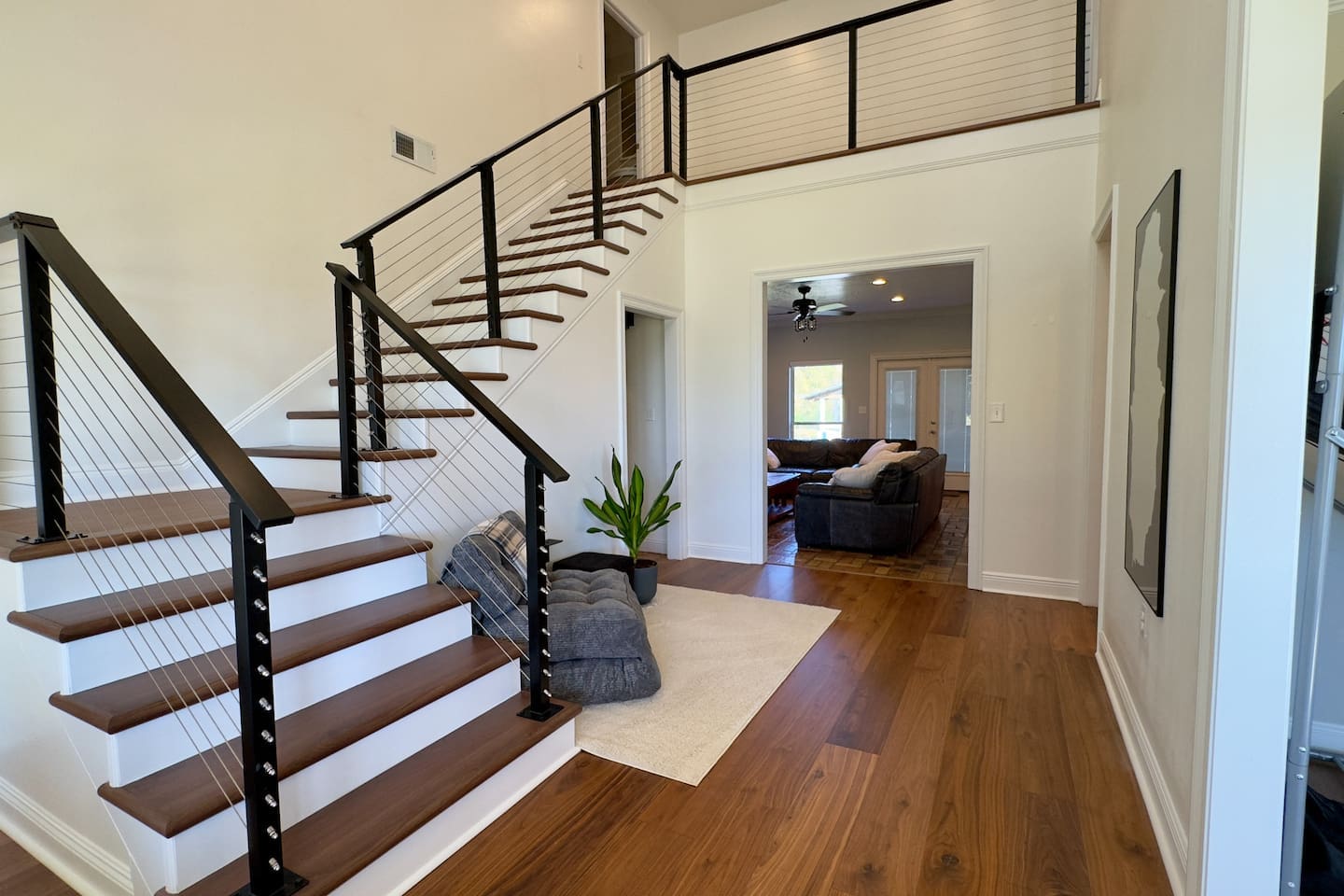 An adjoining living room with dark sofas and large windows connects seamlessly, filling the home with natural light.
