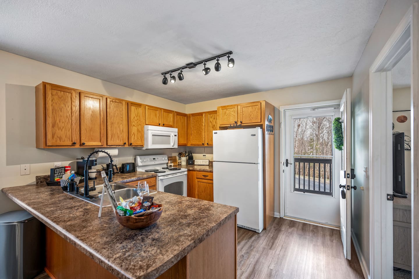 Fully equipped kitchen with modern appliances, ample counter space, and warm wooden cabinetry. Features a spacious island with a deep sink, perfect for meal prep and entertaining. Easy access to the front outdoor deck for fresh air and scenic views.