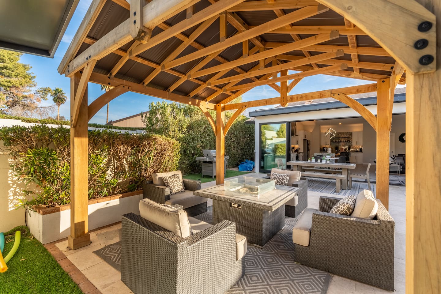 The warm natural wood of the pergola and surrounding hedge create an inviting conversation space anchored by a fire table at its heart.
