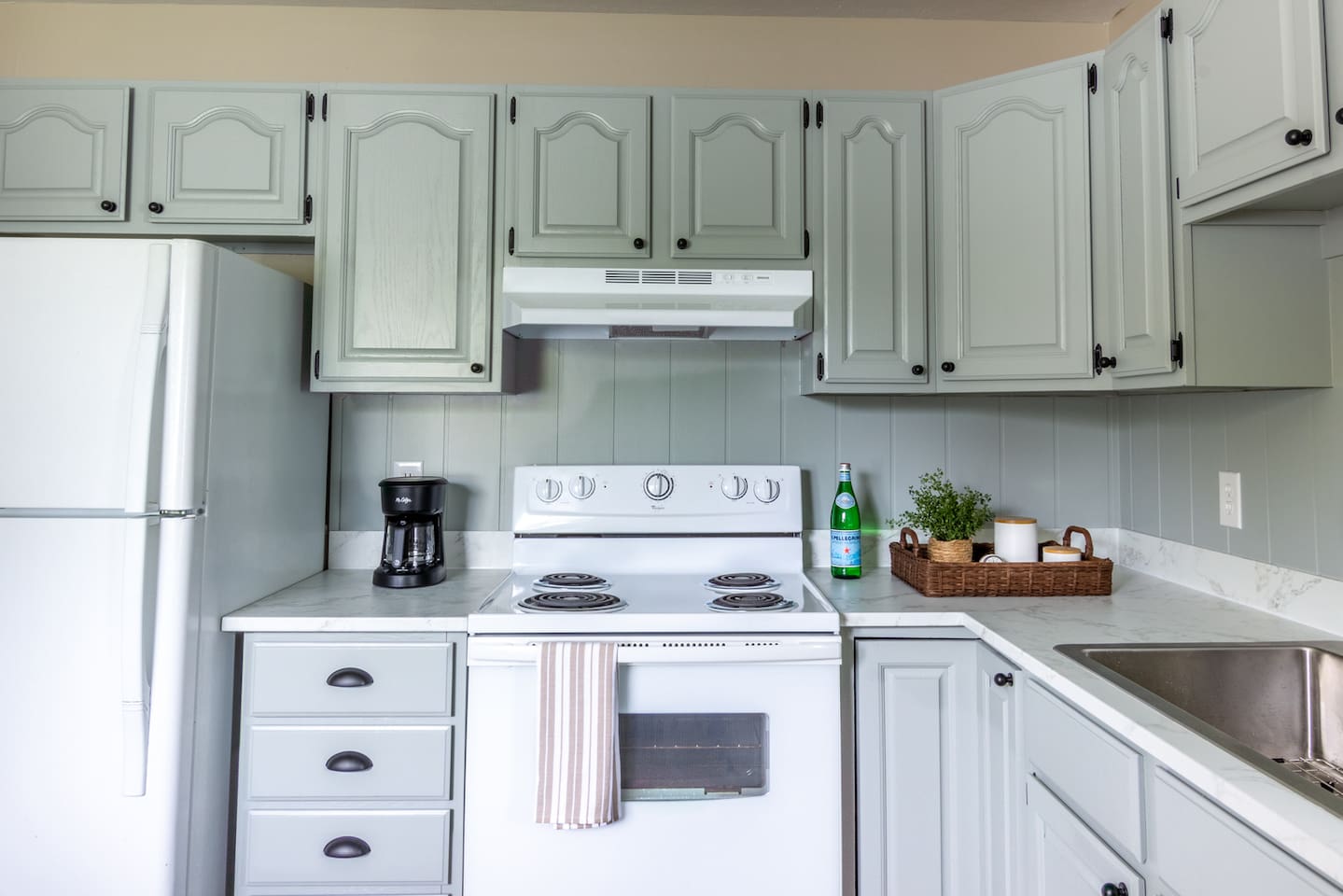 Classic white appliances and soft green cabinetry make the cook space feel bright and welcoming.