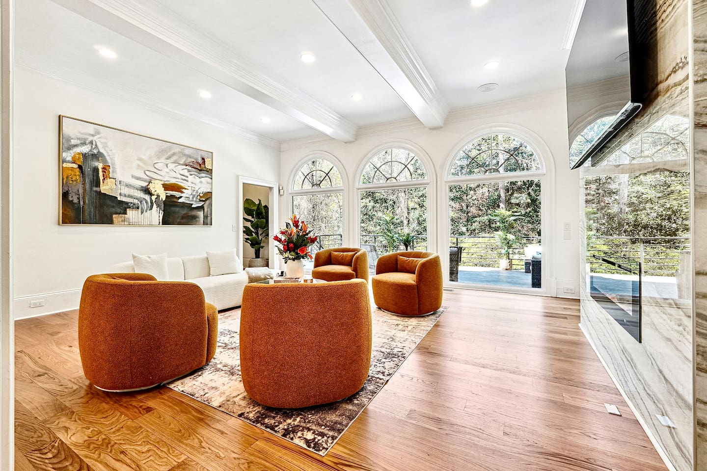 Located straight ahead from the front entry, this main-floor living room showcases a striking modern design with a round shaped contemporary sofa, four orange accent chairs, a smart TV, and a fireplace for a warm, elevated lounge experience.