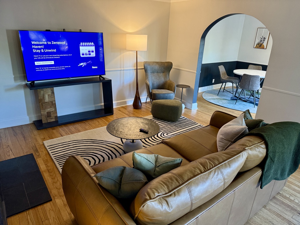 Smart Roku TV with Guest Mode, large couch and comfy reading chair fill the living room space. The TV comes with an HDMI cable to conveniently plug in your gaming consoles.