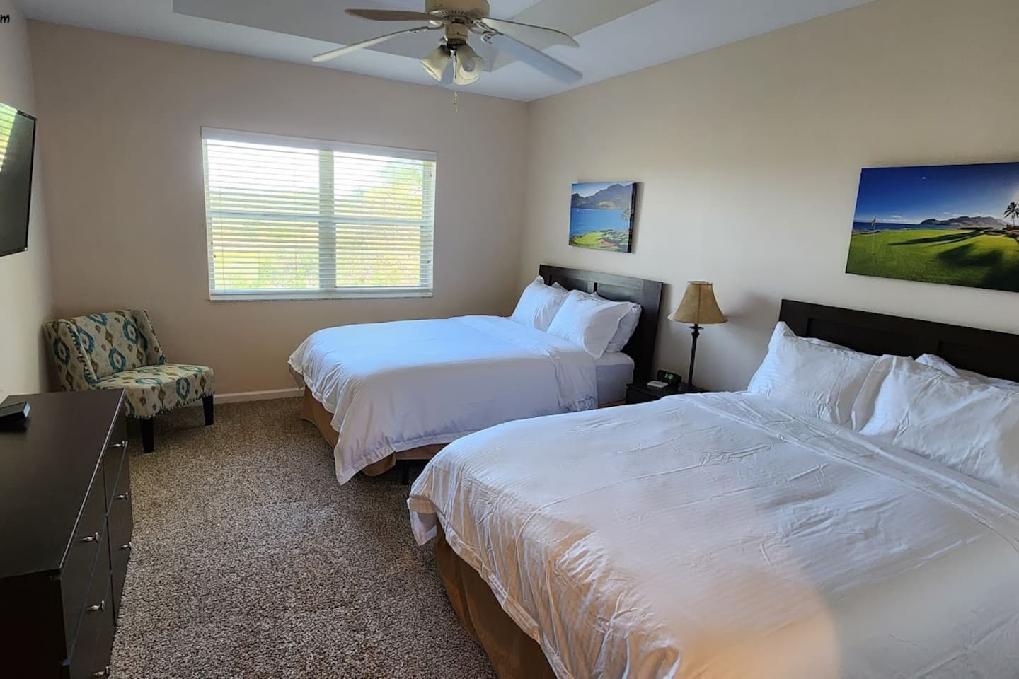 Bright bedroom with two comfortable beds, natural light, ceiling fan, and a cozy seating area.