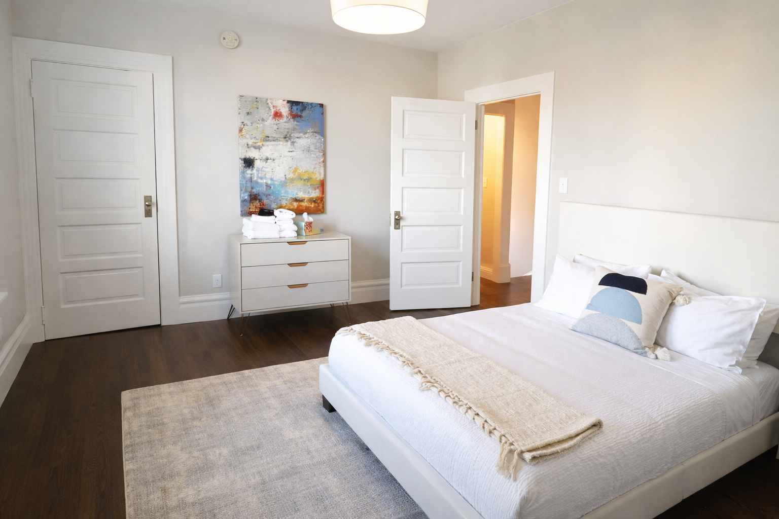 Retreat to the sun-drenched primary bedroom, featuring a comfortable king-size bed, designer art, and warm hardwood floors.