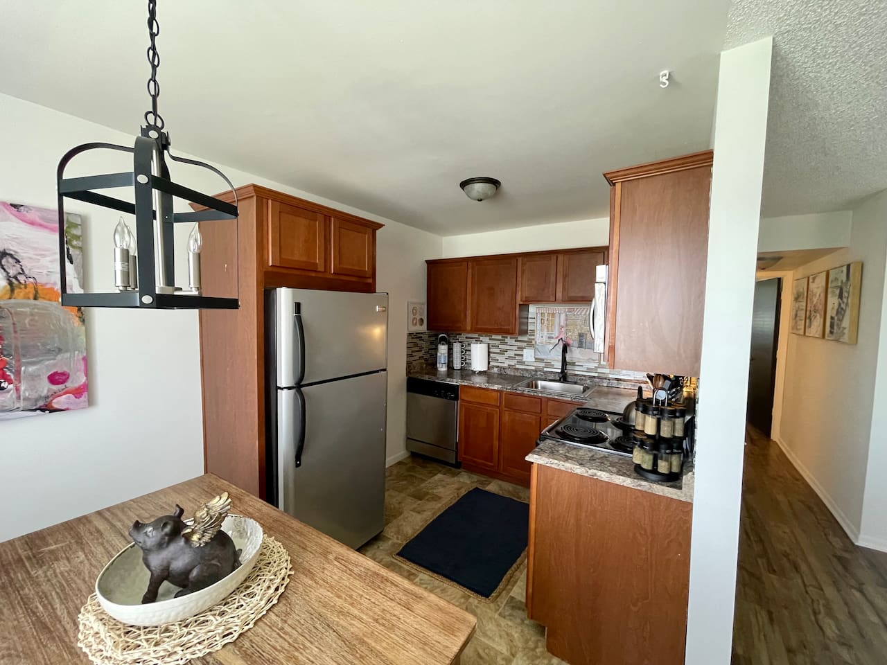 Stylish kitchen featuring stainless steel appliances, granite-look countertops, and warm wood cabinetry. The space opens to a cozy dining nook with unique decor, perfect for enjoying meals or morning coffee in comfort.