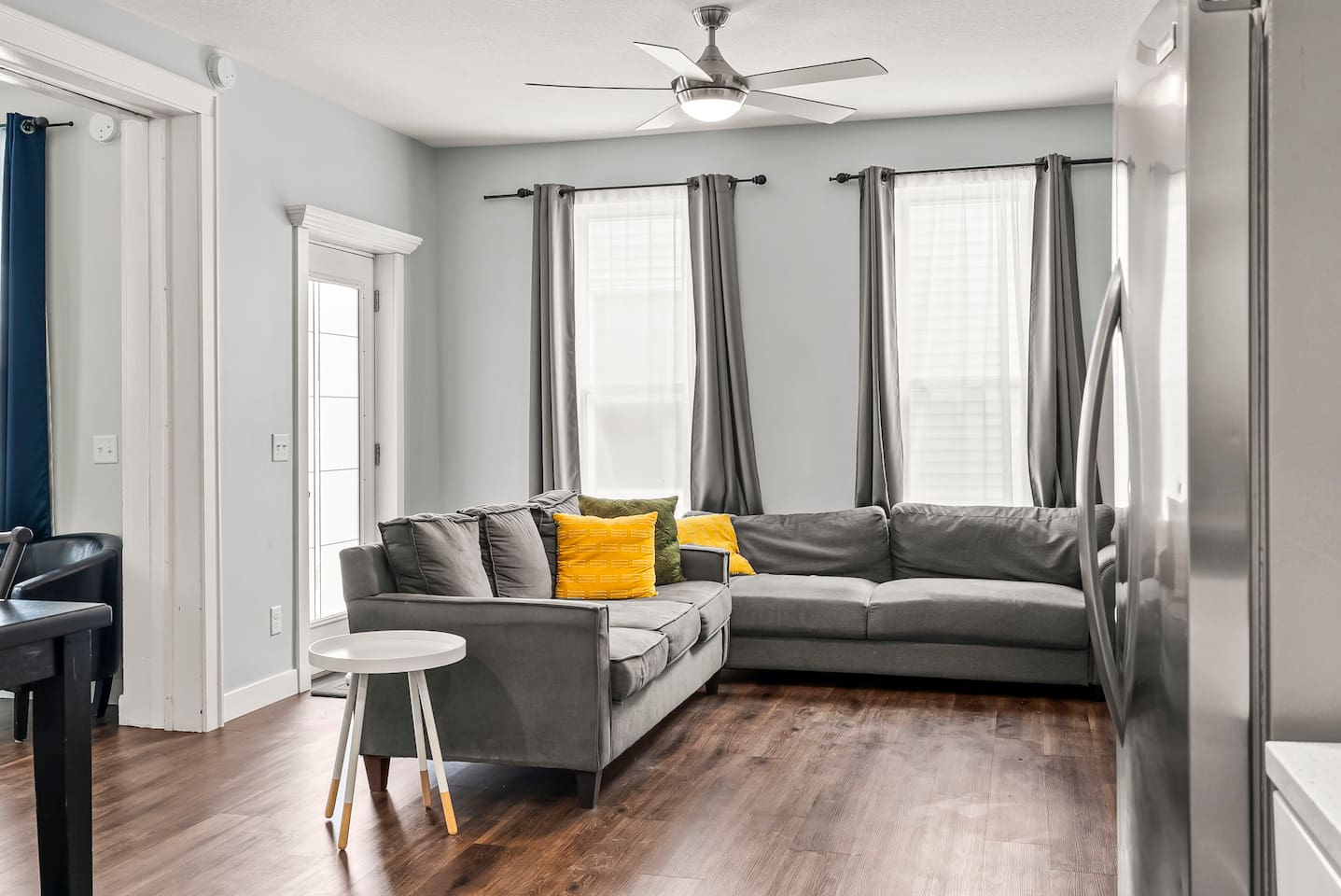 Modern yet cozy living space with ample seating, ceiling fan, and bright windows — perfect for groups or extended stays.