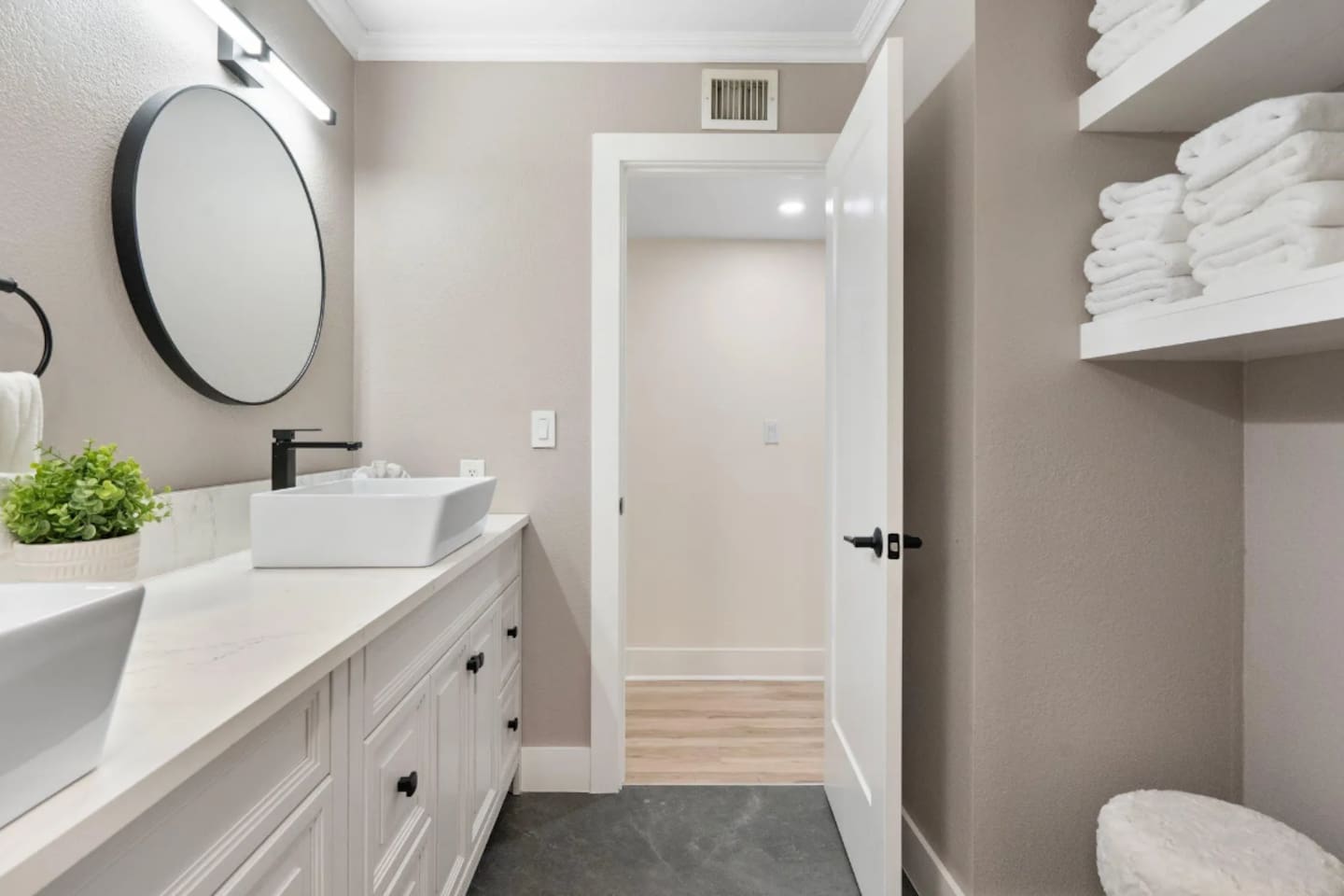 A crisp white vanity with a vessel sink and round mirror keeps things simple and bright, while open shelving means towels are always within reach.