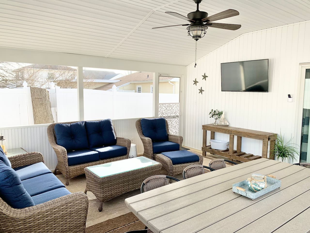 Experience the best of indoor-outdoor living in our screened-in sunroom. Kick back on navy wicker seating to watch the game or enjoy a meal at the large dining table—all while staying protected from the elements in a bright, coastal setting.