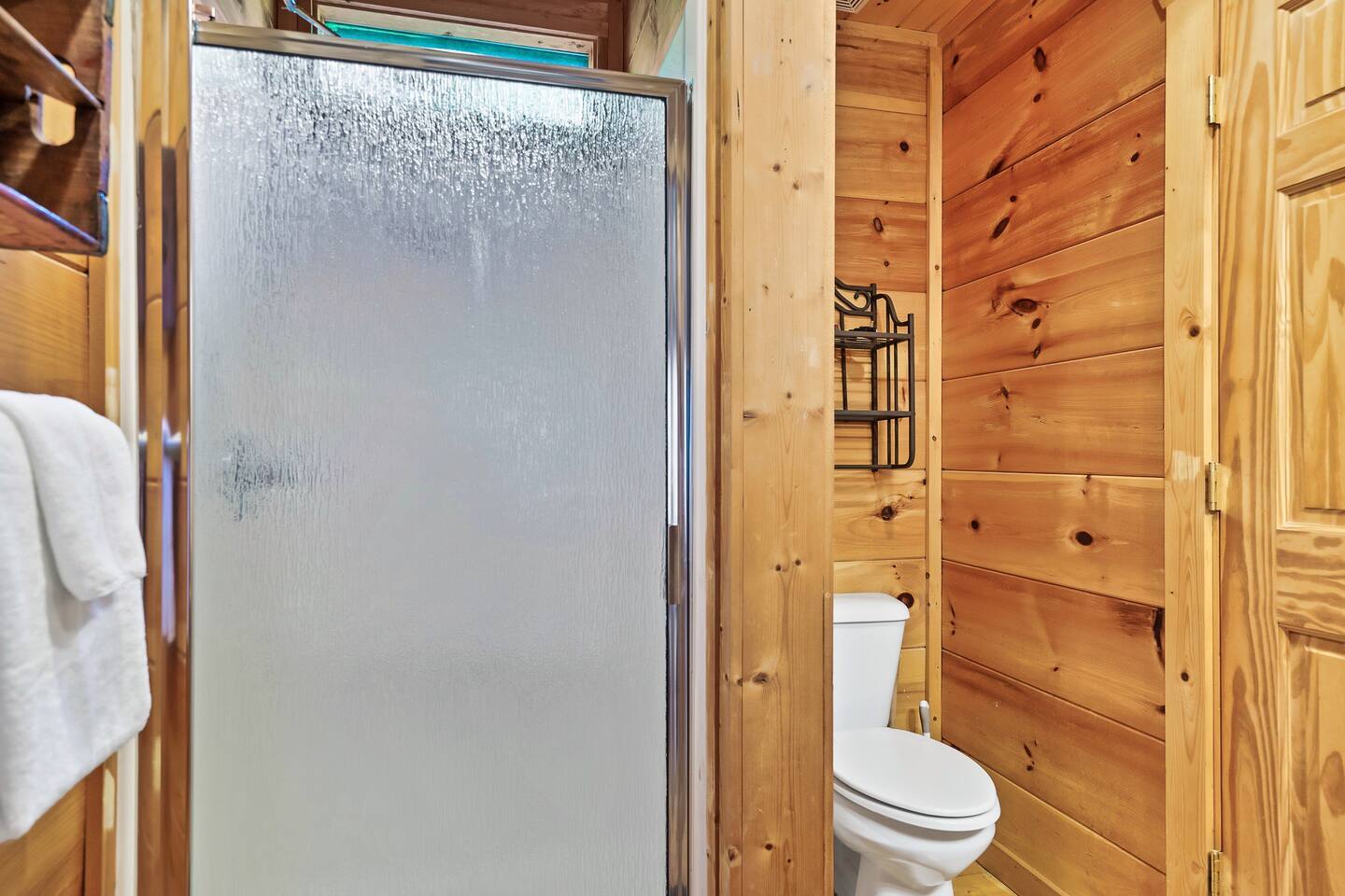 This compact bathroom combines a sleek frosted glass shower with natural wood tones, offering a functional and inviting space with an elegant yet rustic vibe.