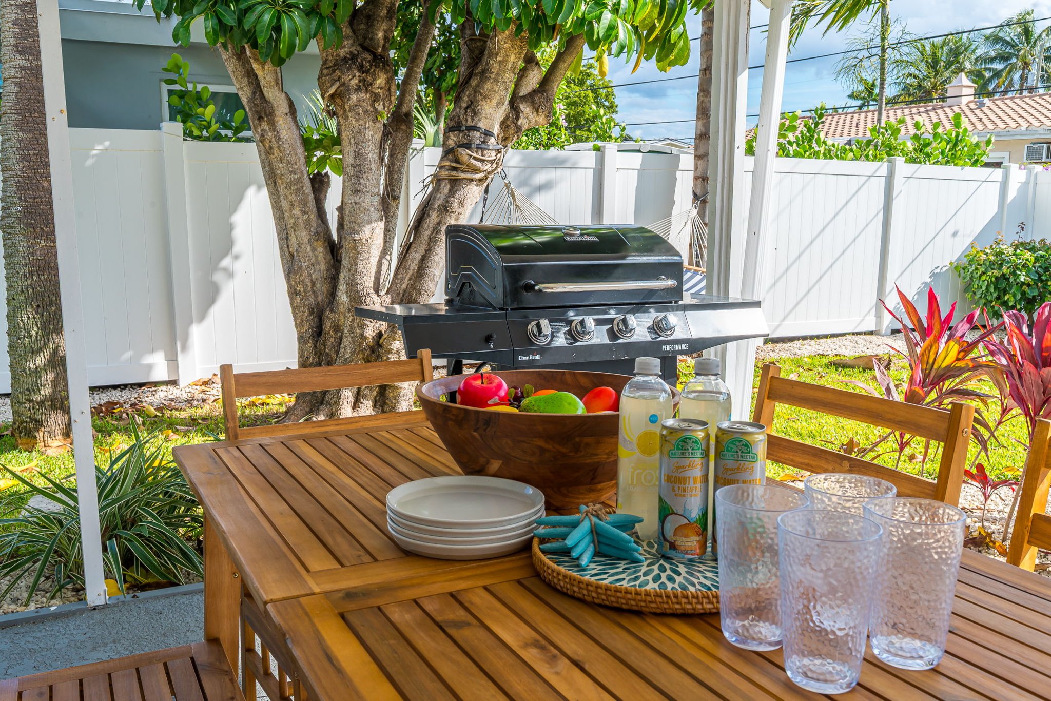 A serene covered patio with chic seating, alfresco dining, a gas grill, and a two-person hammock, all framed by a mix of manicured turf and lush lawn—your private outdoor retreat.