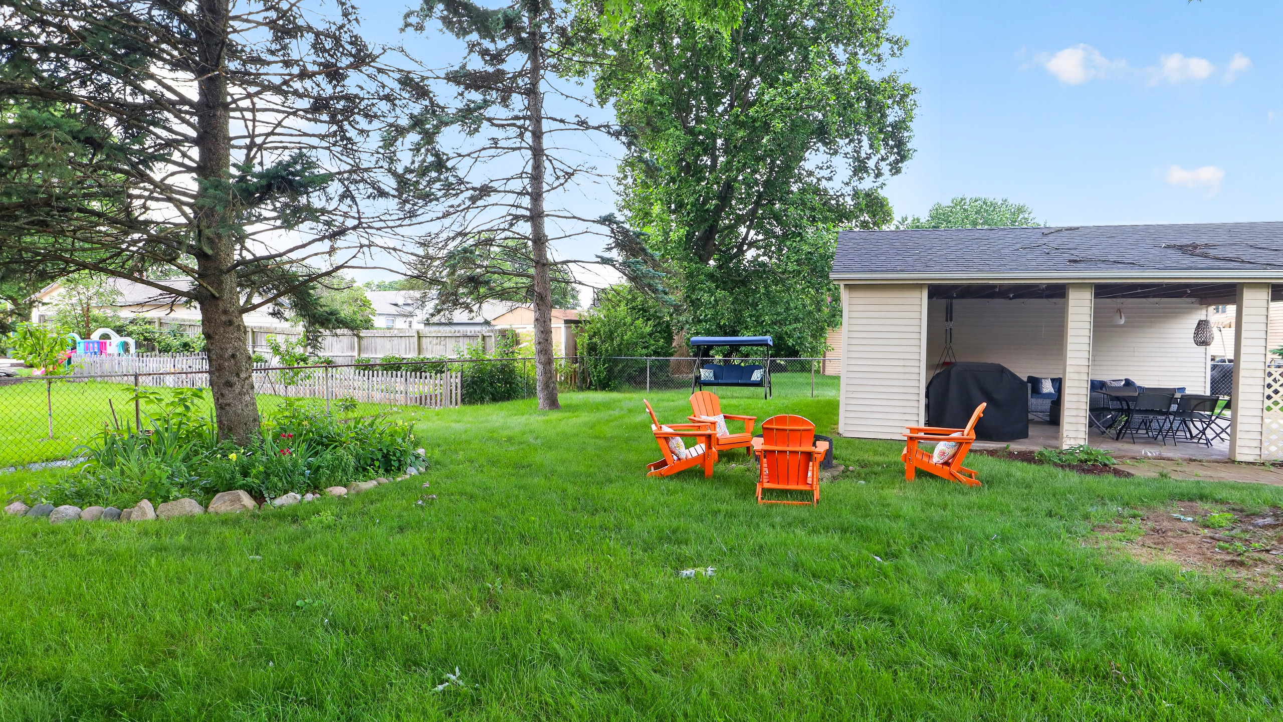Flat, grassy backyard with a fire pit, glider swing, and room to relax or play.