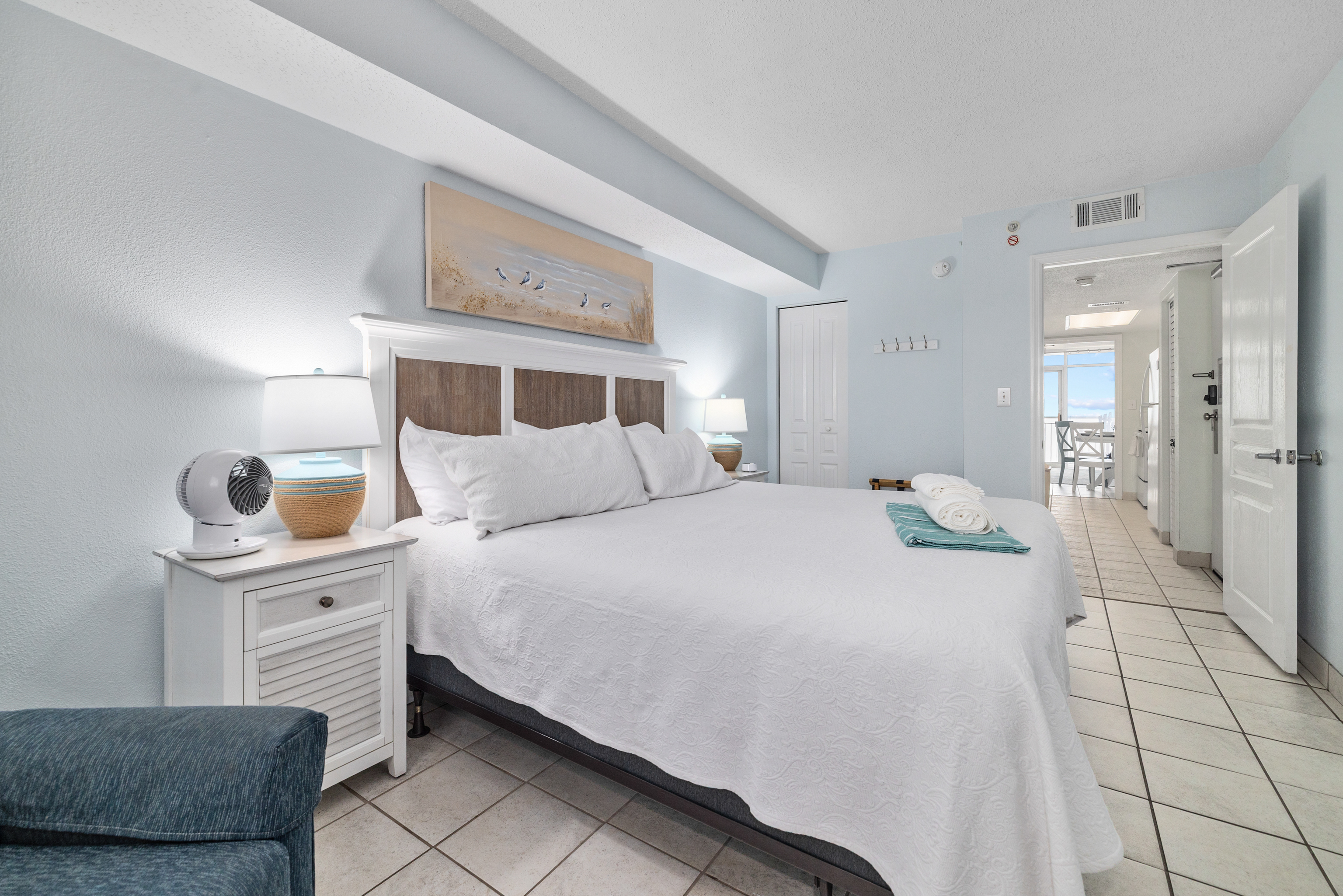 Spacious king bedroom with plush bedding, coastal décor, and natural light streaming in.