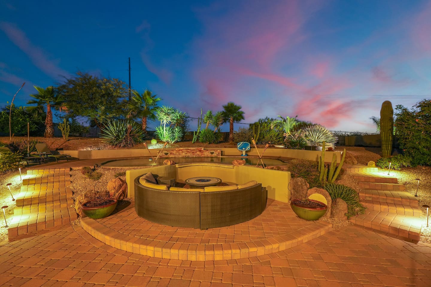 Evening ambiance at the fire pit with soft lighting, layered stonework, and a stunning desert sunset.
