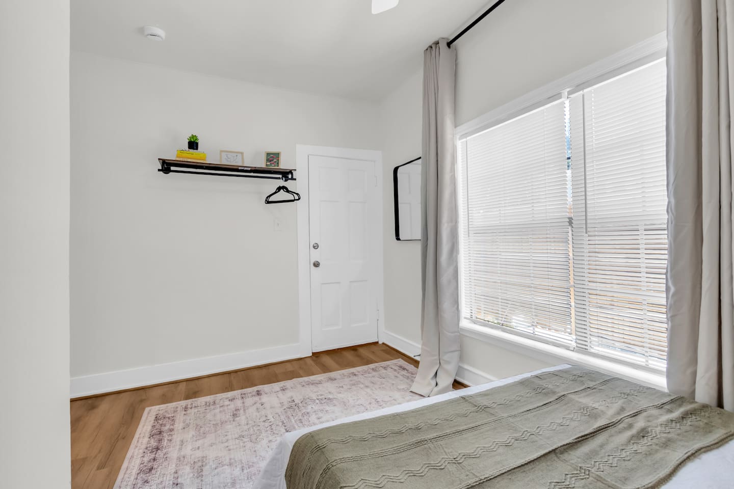 Queen bedroom with exposed closet with hangers, room darkening shades, and a large window.