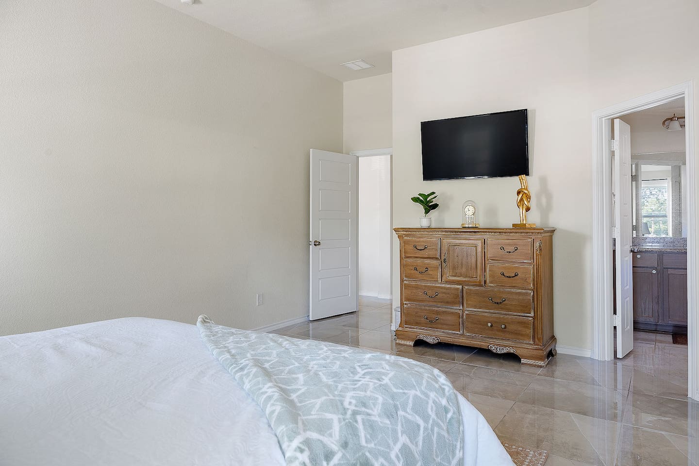 Experience comfort in this bedroom with a mounted TV, classic wooden dresser, and elegant decor accents.
