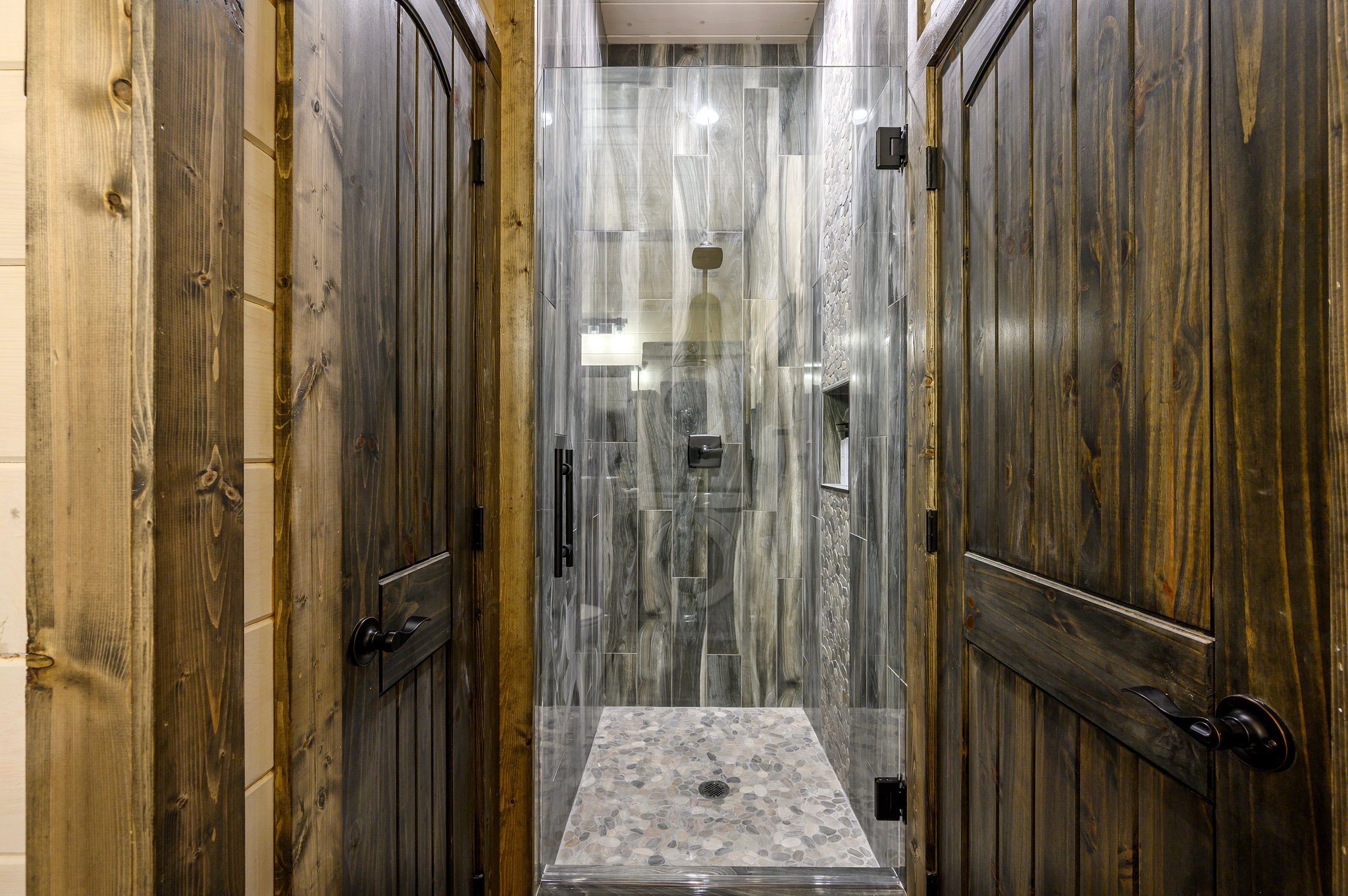 Spa-inspired walk-in shower framed by warm, reclaimed wood doors.
