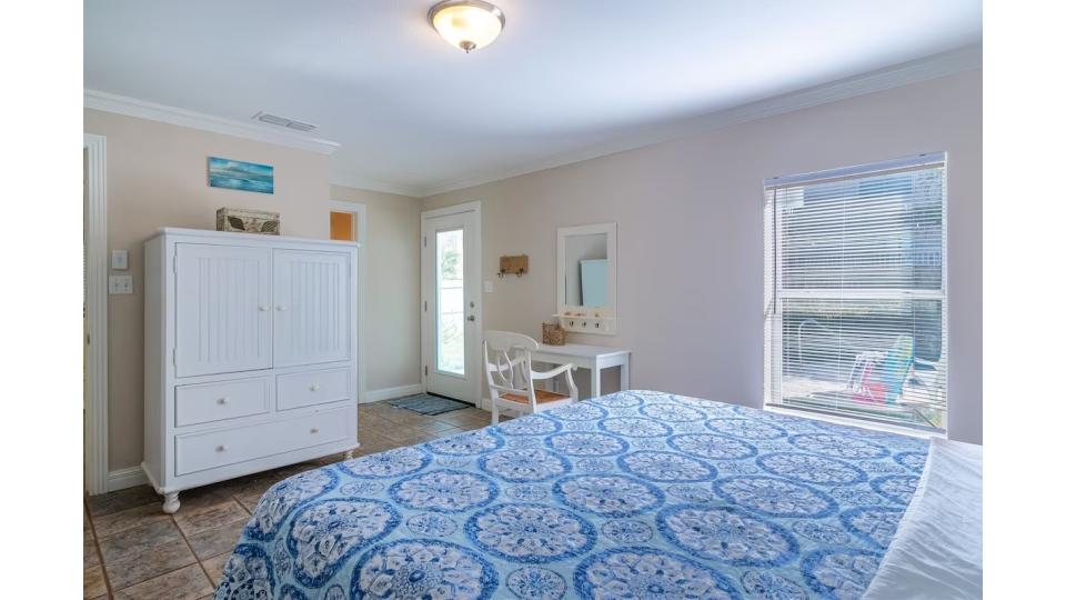 King Master Suite with direct pool access. Wake up to natural light streaming through large windows, step outside to your private tropical backyard, or enjoy in-room entertainment on your personal HDTV. Coastal blue bedding and beach-inspired decor complet