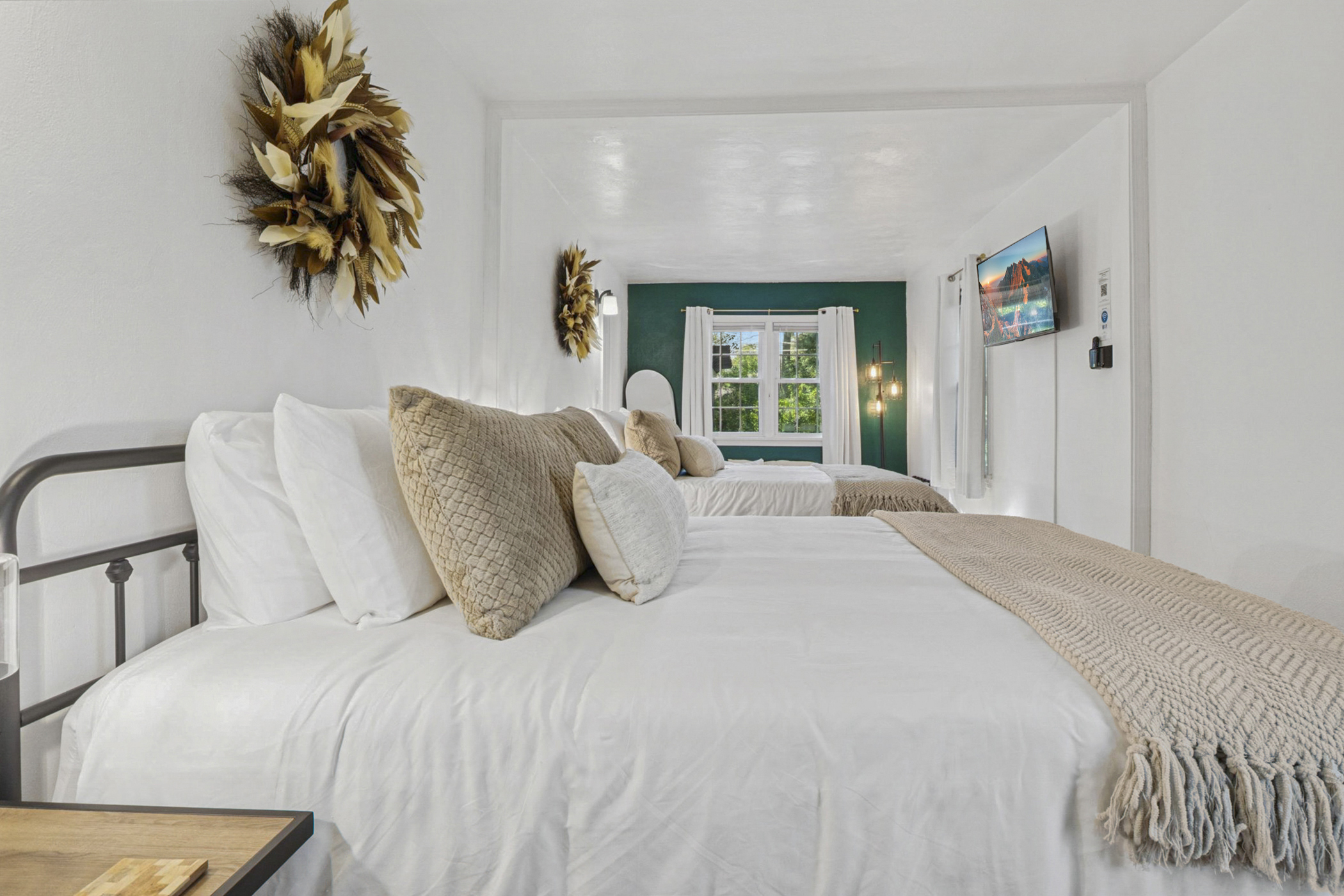 Feather wreaths crown each queen bed, adding soft style. Cozy blankets, plush pillows, and bedside touches create a warm South Bend guest retreat near Notre Dame—perfect for restful nights.