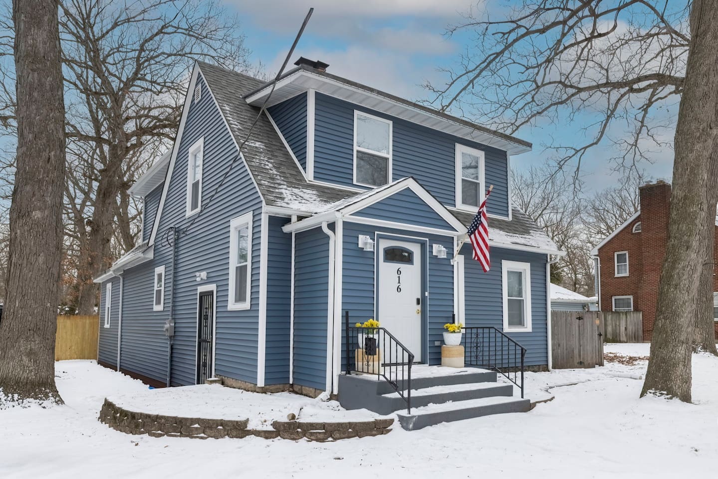 A charming coastal-style home with blue siding and white trim, made even cozier by a winter snowfall.