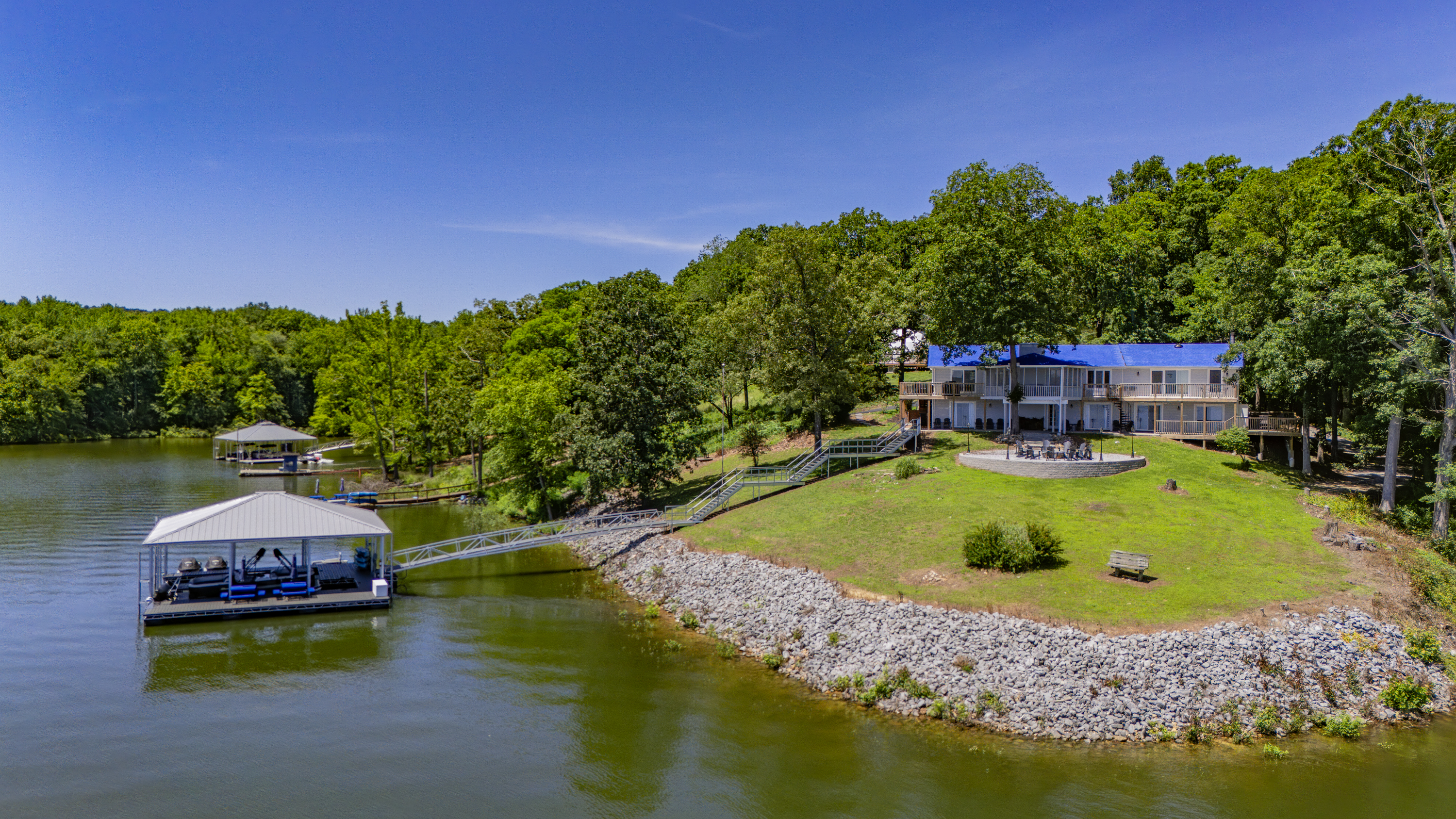 The home sits along a broad waterfront lawn with direct lake access, a firepit, and its own covered dock.