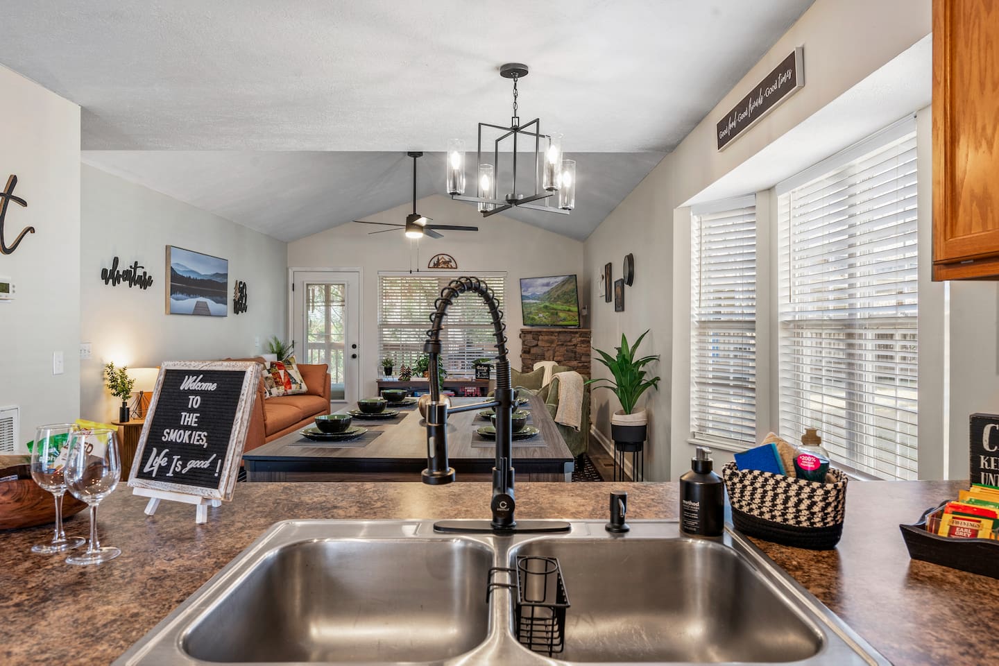 Modern kitchen view with a double sink, stylish faucet, and open sightlines to a cozy living and dining area—perfect for entertaining or relaxing at home.