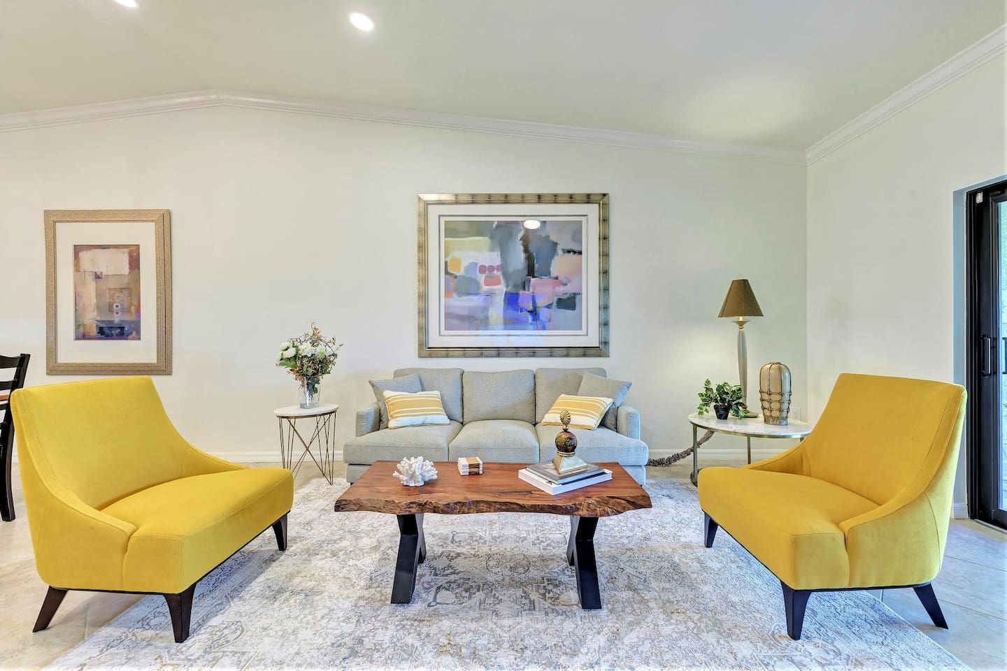 A cozy living room with a gray couch, yellow accent chairs, wooden coffee table and abstract paint above the table. 
