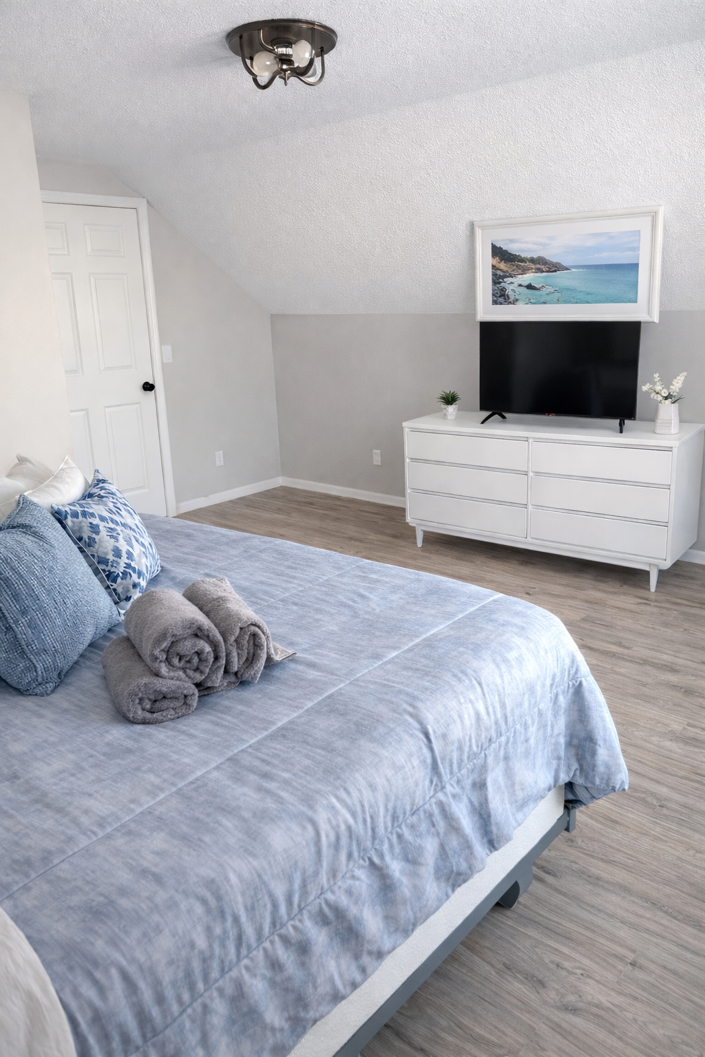 “Bright and airy attic bedroom featuring a plush queen bed, soft linens, and a Smart TV for relaxing nights in. The neutral tones and sloped ceilings create a cozy yet spacious retreat.”