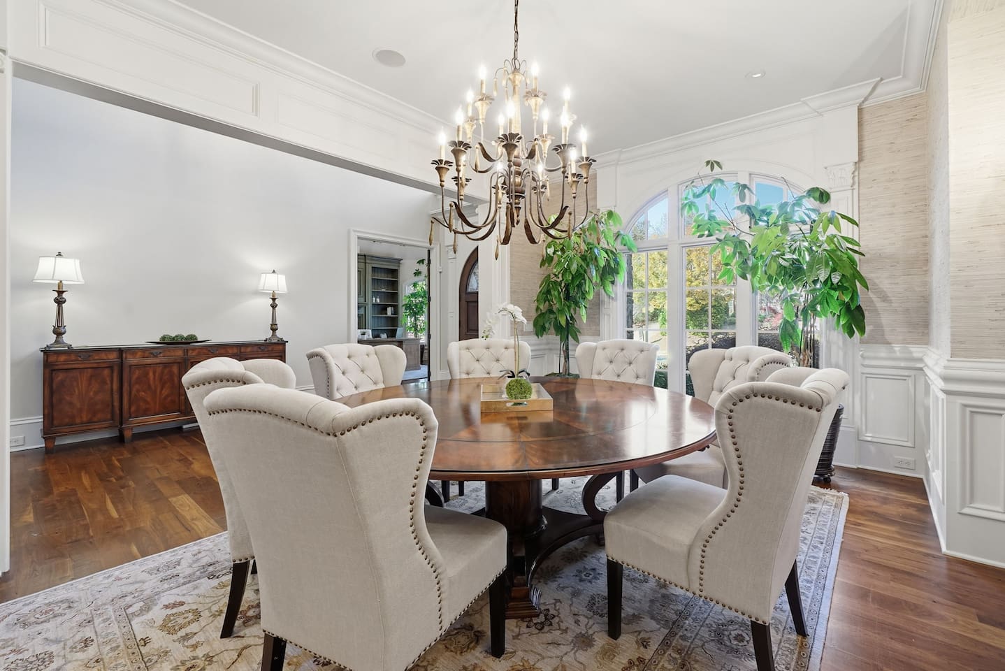 Spacious main dining room to the left of the foyer, featuring a chandelier, seating for seven, and lush green plants. A bright, welcoming space perfect for shared meals or special gatherings.