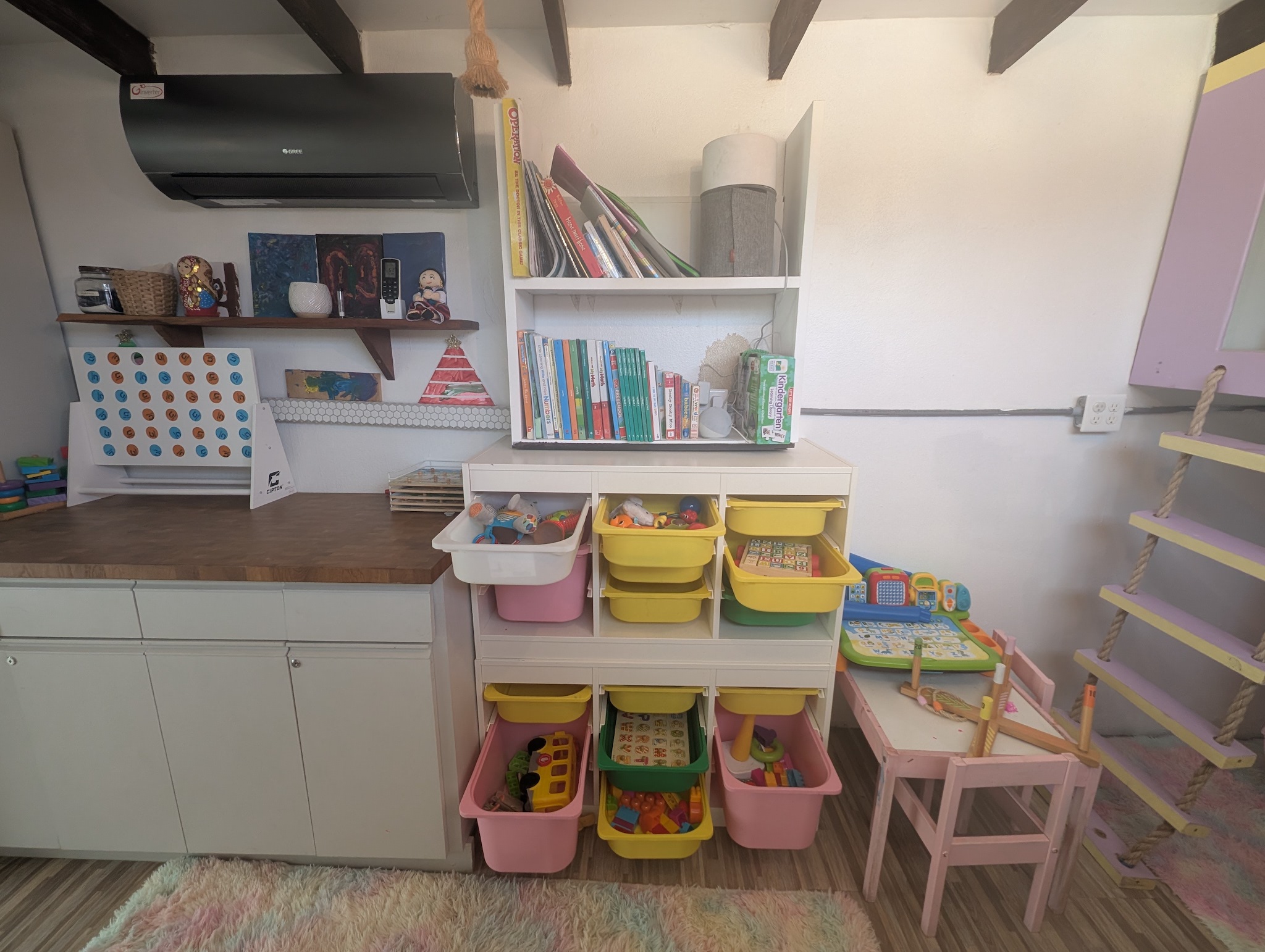 Indoor kids toy and craft station at Villa Coral featuring organized bins with toddler learning toys, books, a large wooden Connect Four game, and a small pink activities table in Dorado, Puerto Rico.