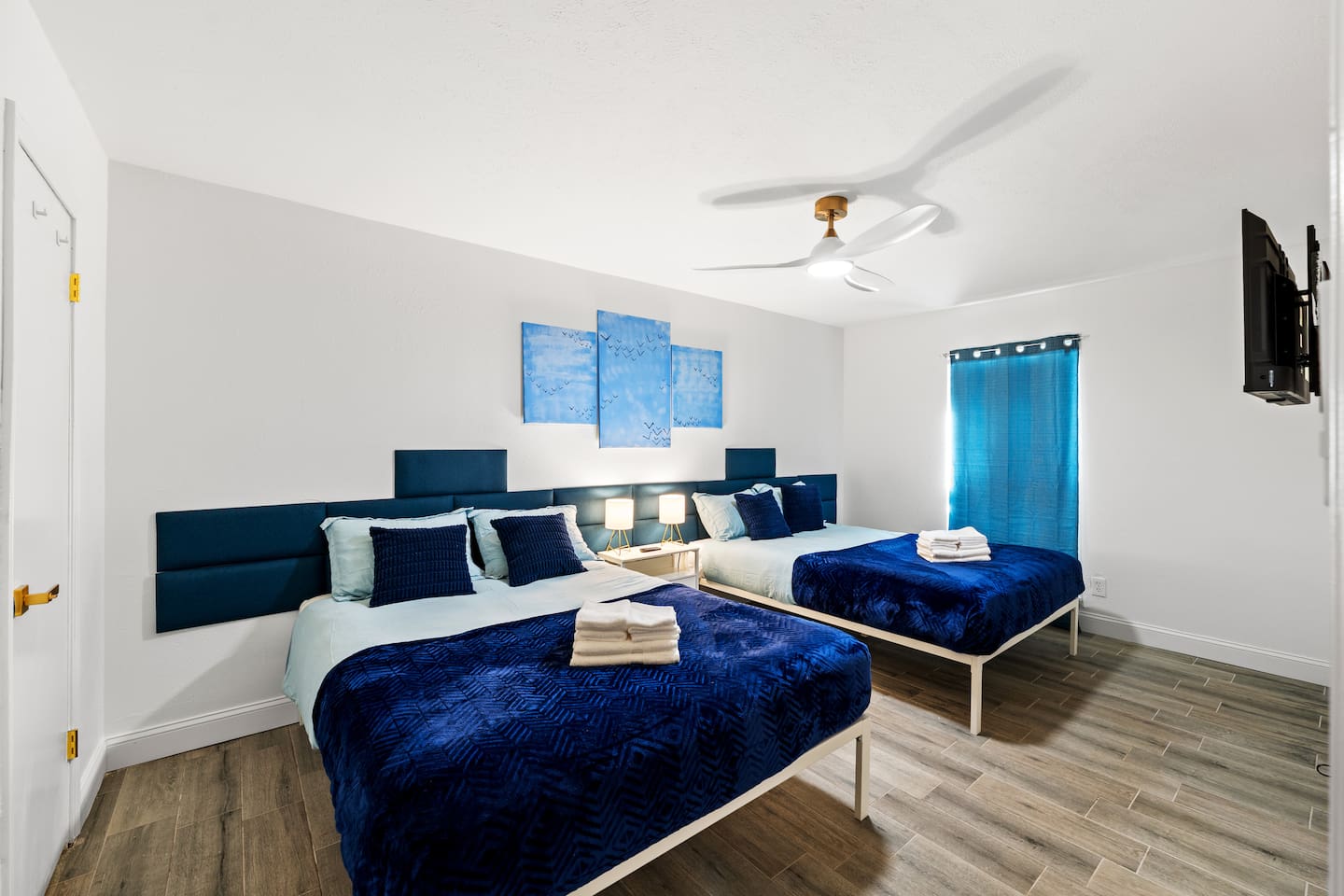 Spacious bedroom with two plush queen beds, blackout curtains, and a smart TV—ideal for families or groups to unwind in comfort.