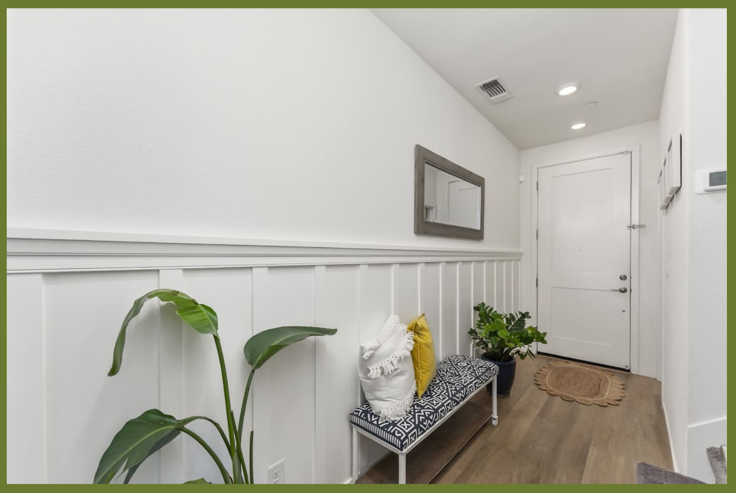 Entry hallway with bench seating, wall mirror, greenery, and a clean arrival path into the home.