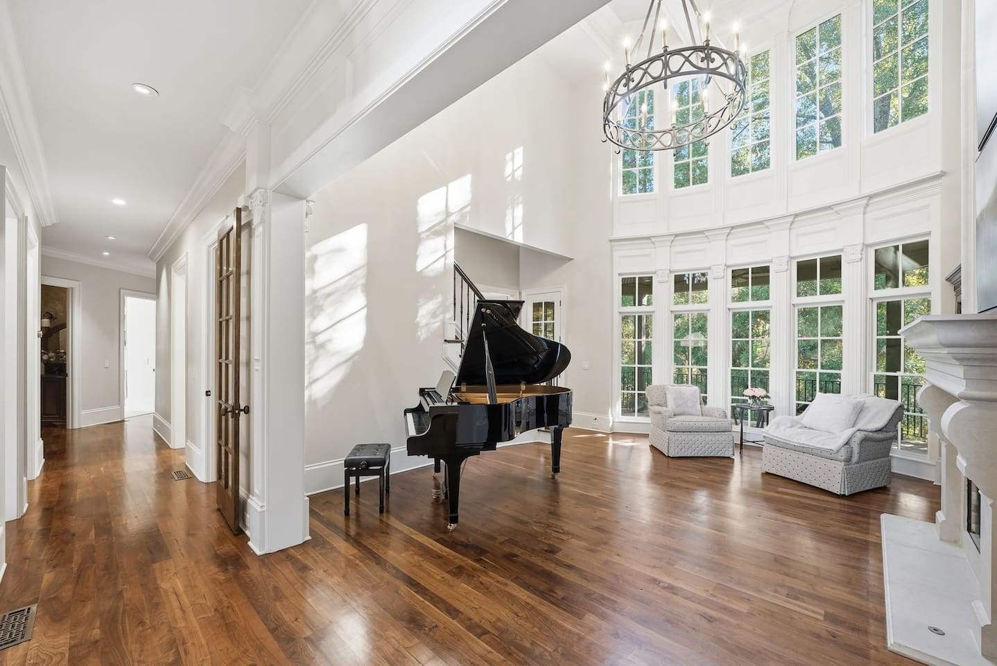 Beautiful entry sitting room with a grand piano, warm fireplace, tall windows, and two comfortable chairs. A bright, serene spot to unwind or enjoy quiet moments.