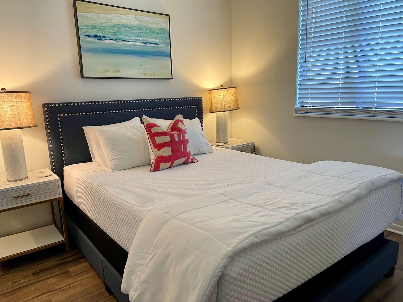 Serene and stylish bedroom with a plush king bed, crisp white linens, and calming coastal decor. Enjoy the glow of warm bedside lighting and blackout blinds for restful sleep—your perfect retreat after a day of adventure or work.