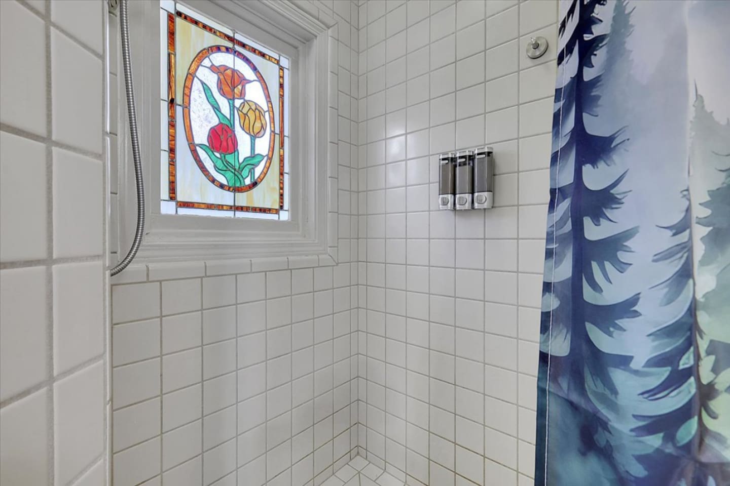 Full Bathroom 1 shower with tiled walls, stained-glass window detail, and shower essentials provided.
