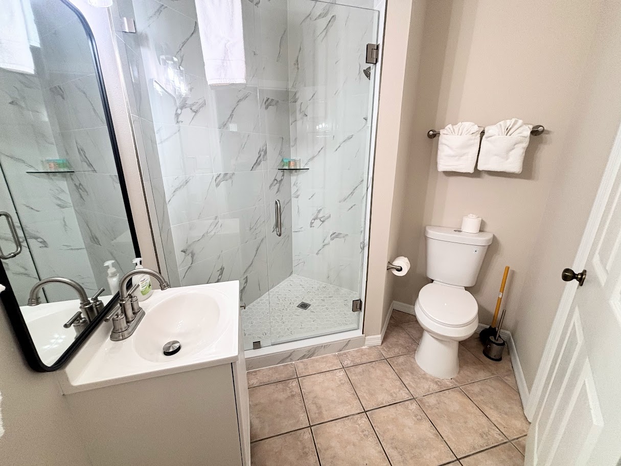Updated bathroom featuring a glass-enclosed walk-in shower, vanity, toilet, and tile flooring.